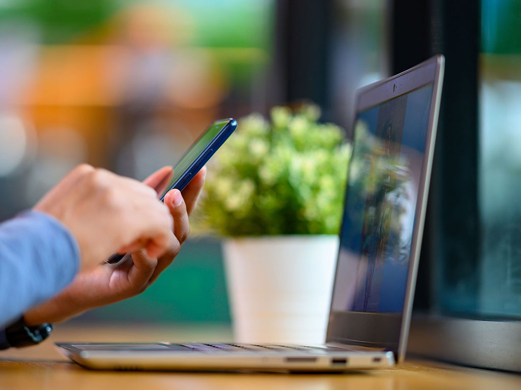 Person using phone with a laptop