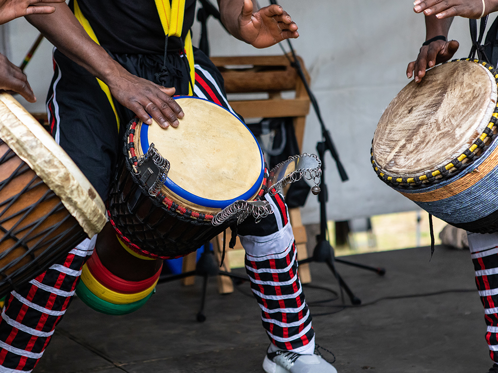 A group of musicians passionately playing drums on a stage, showcasing their rhythmic skills in a lively performance.