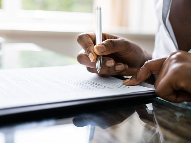 A close-up image capturing the hands of an African American woman as she signs a document with a pen.