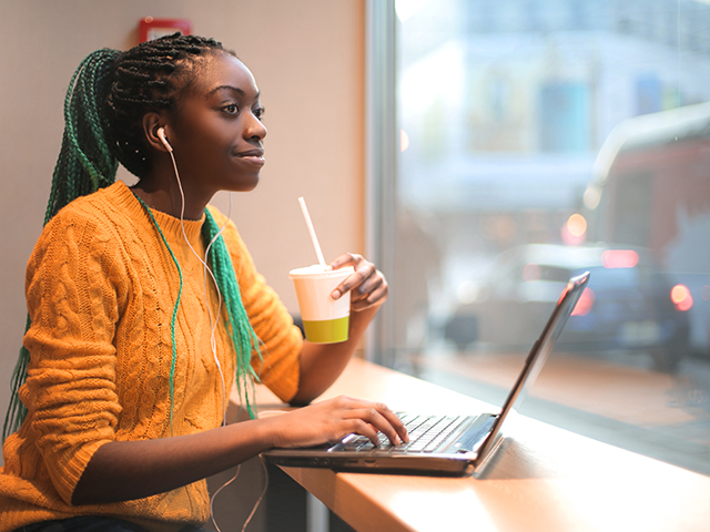 Young black girl, earbuds in, listening to music and using her laptop