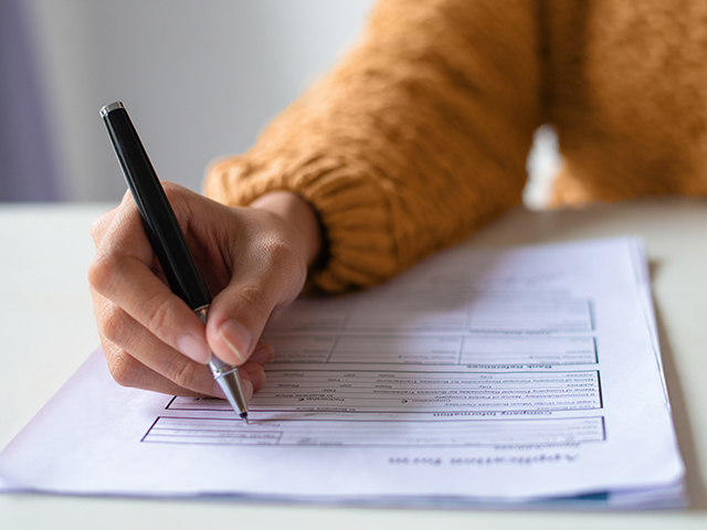 Hand holding a black pen, filling out froms