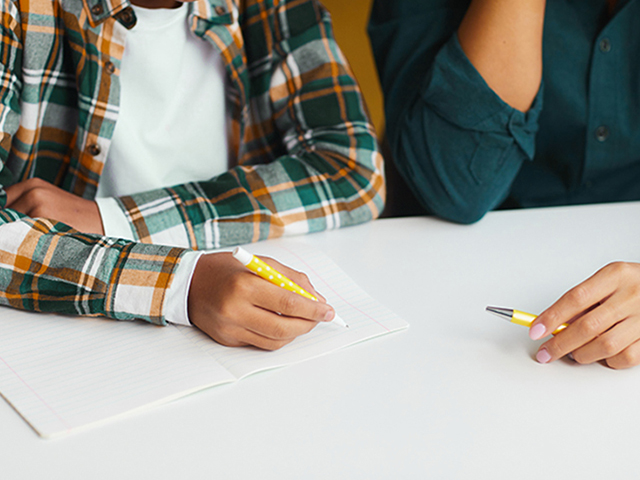 Close up of hands doing school work. Student and Tutor