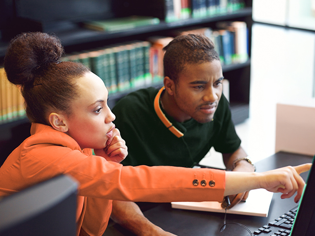 young man and woman looking at computer in library