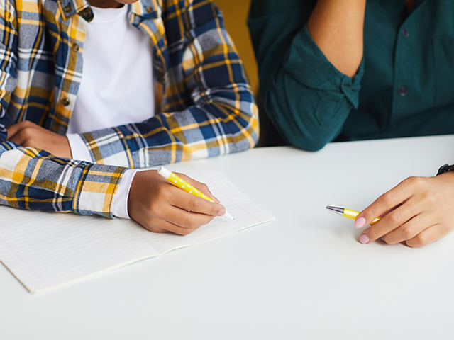 Close up of hands doing school work. Student and Tutor