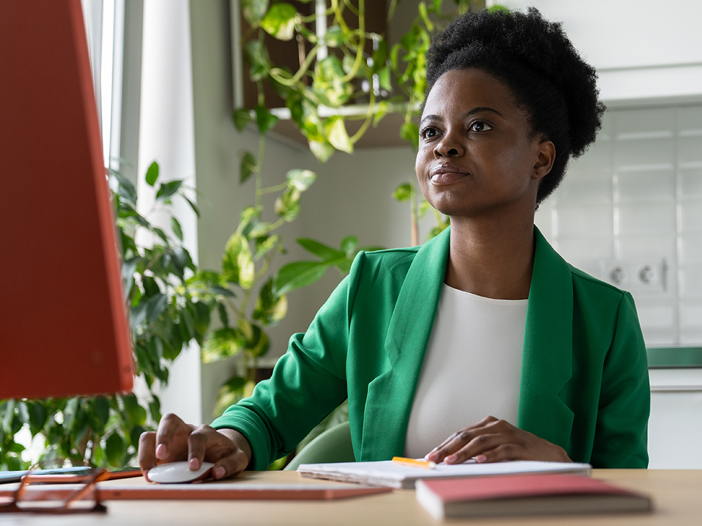 A professional young woman in a green blazer sitting at her desk looking at computer