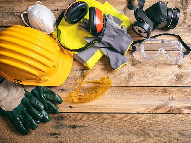 Top view of  construction site safety items, including a Protective hard hat, headphones, gloves, glasses and masks on wooden background