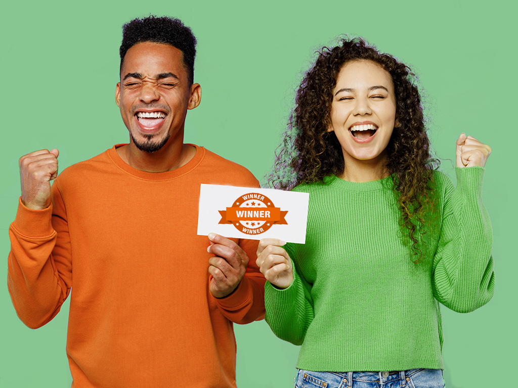 A young man and a young woman are smiling and proudly holding up a paper certificate signifying them as the winners of a drawing.