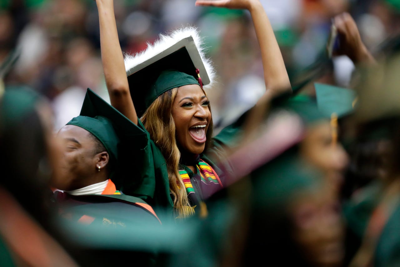 A happy female student in cap and gown cheering during comemncment