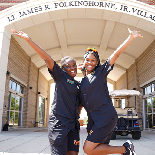 two students jumping in the air in front of Polkinghorne Village arch