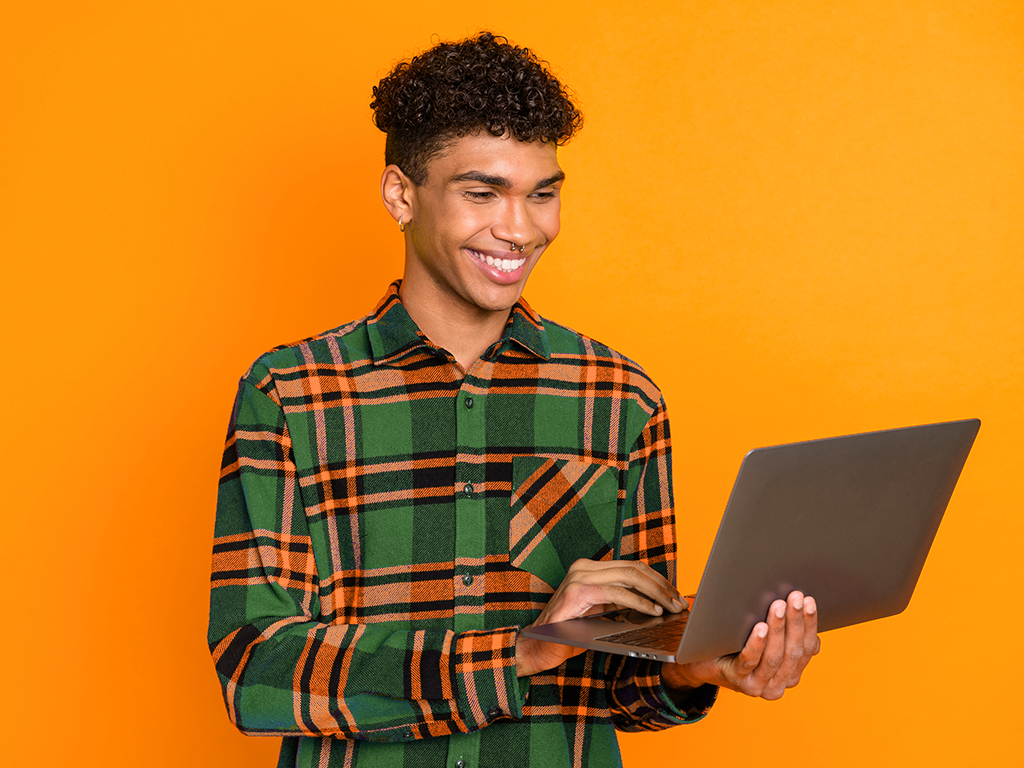 Male student holding and using a silver laptop