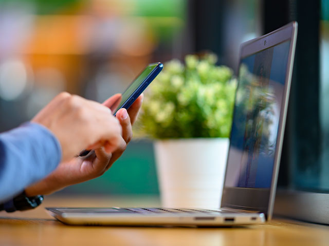 Person holding a cell phone in front of a laptop