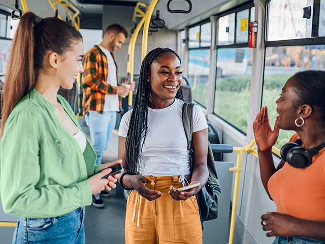 Three girls standing and talking on a city bus