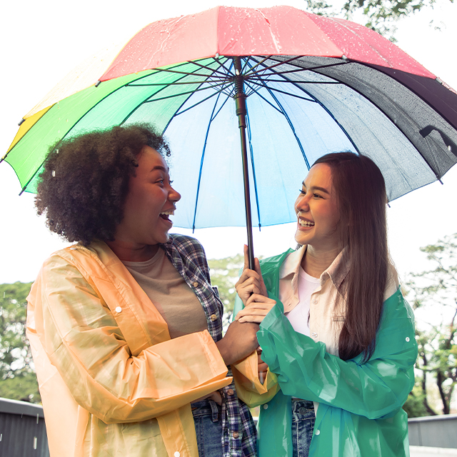 Two young woman sharing an umberella after being caught in the rain