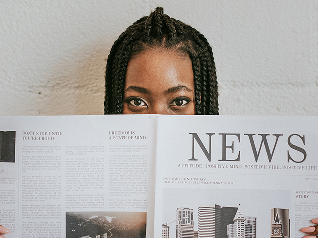 girl holding a newspaper to cover the bottom half of her face