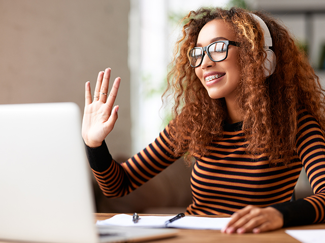 African-american young woman using laptop, waving and looking at screen during an online meeting video call