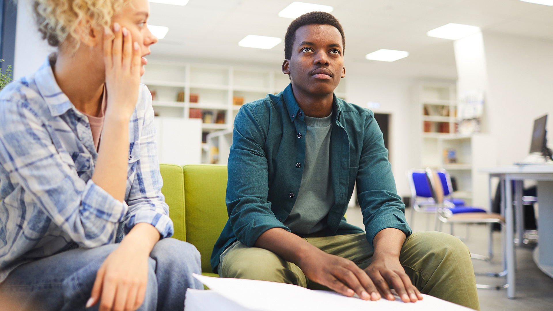 African-American young man reading braille while studying with seeing friend in school library